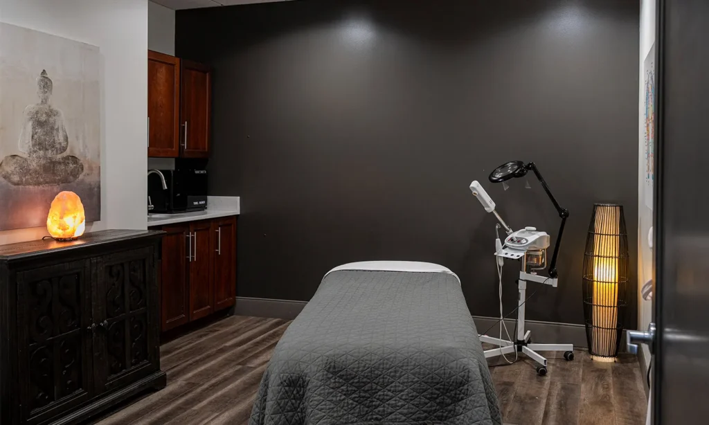 - Bella Capelli Sanctuario in Westlake, OH A spa treatment room with a massage table, dark gray walls, wooden cabinets, a salt lamp, and various spa equipment. - Bella Capelli Sanctuario in Westlake, OH