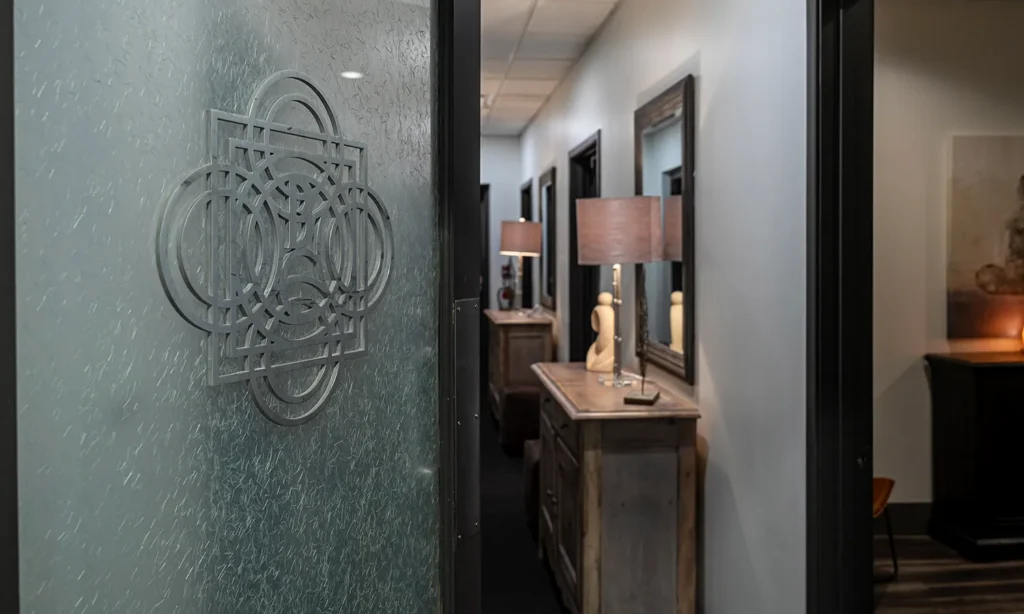 - Bella Capelli Sanctuario in Westlake, OH Frosted glass door with geometric design opens to a hallway featuring wooden furniture, decorative lamps, and framed wall art. - Bella Capelli Sanctuario in Westlake, OH