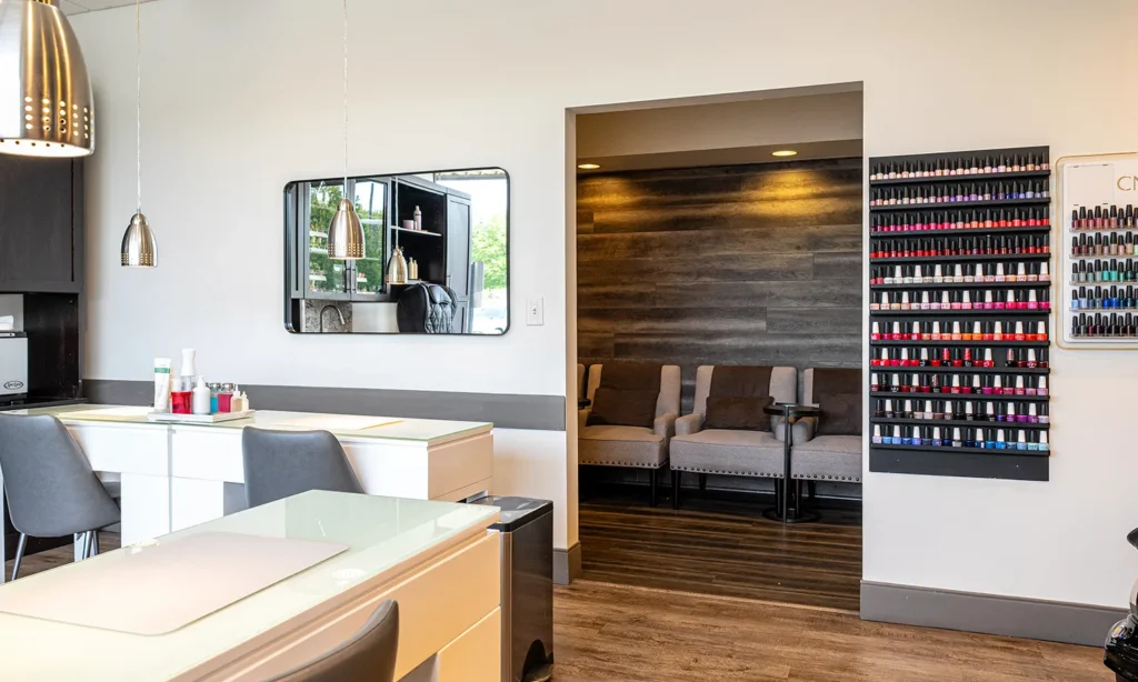 - Bella Capelli Sanctuario in Westlake, OH Modern nail salon interior with manicure stations in the foreground, a seating area in an alcove, and a wall display of colorful nail polish bottles. - Bella Capelli Sanctuario in Westlake, OH