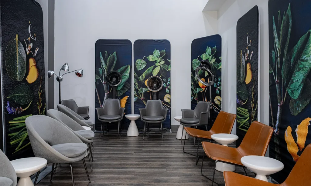 - Bella Capelli Sanctuario in Westlake, OH A salon waiting area with gray chairs, brown leather chairs, and large botanical-themed wall art. - Bella Capelli Sanctuario in Westlake, OH