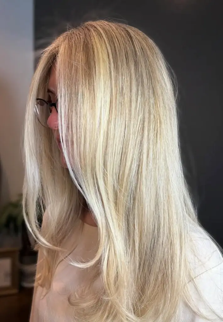 - Bella Capelli Sanctuario in Westlake, OH Person with straight, long, light blonde hair and glasses, viewed from the side, wearing a light-colored top against a dark background. - Bella Capelli Sanctuario in Westlake, OH