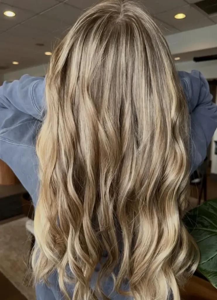 - Bella Capelli Sanctuario in Westlake, OH Person with long, wavy, blonde hair seen from the back, wearing a blue top in an indoor setting. - Bella Capelli Sanctuario in Westlake, OH